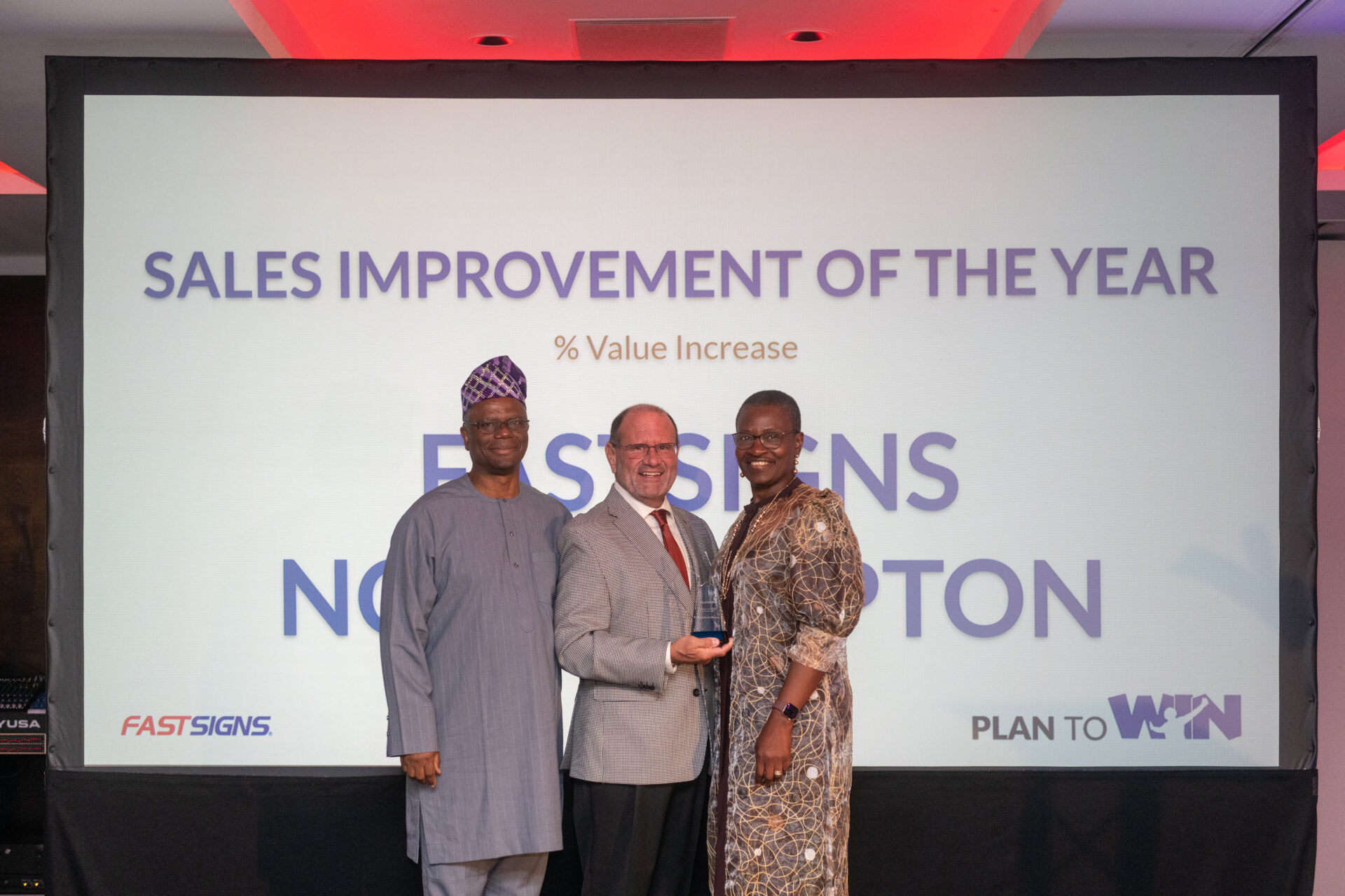 Tunde and Laide Sodipo on stage with Jime How at the 2026 FASTSIGNS UK Convention collecting their award.